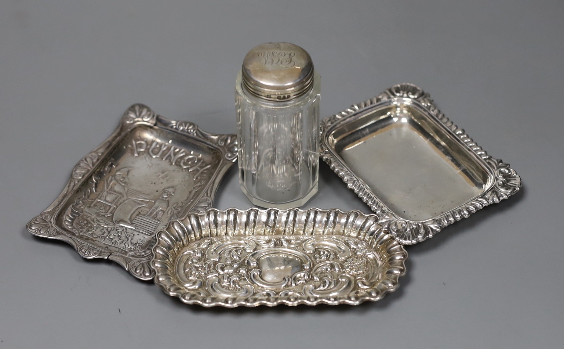 A late Victorian repousse silver 'Mr Punch' pin-tray, 10 x 8cm., Saunders & Shepherd, Birmingham, 1894, 10.7cm, one other silver dish, a silver mounted toilet jar and a plated small dish.